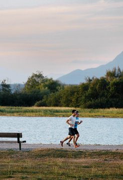 Two people jogging along a Dyke in Richmond with water and greenery in the background